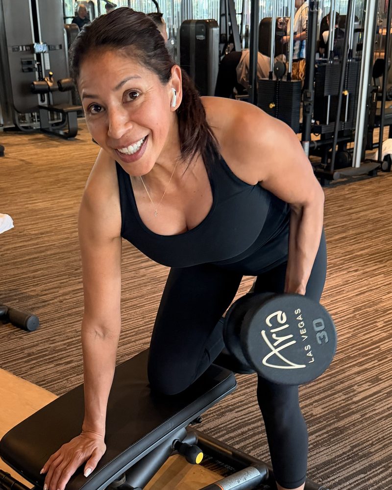 Elvia entrenando fuerza con mancuerna en el gimnasio, sonriendo